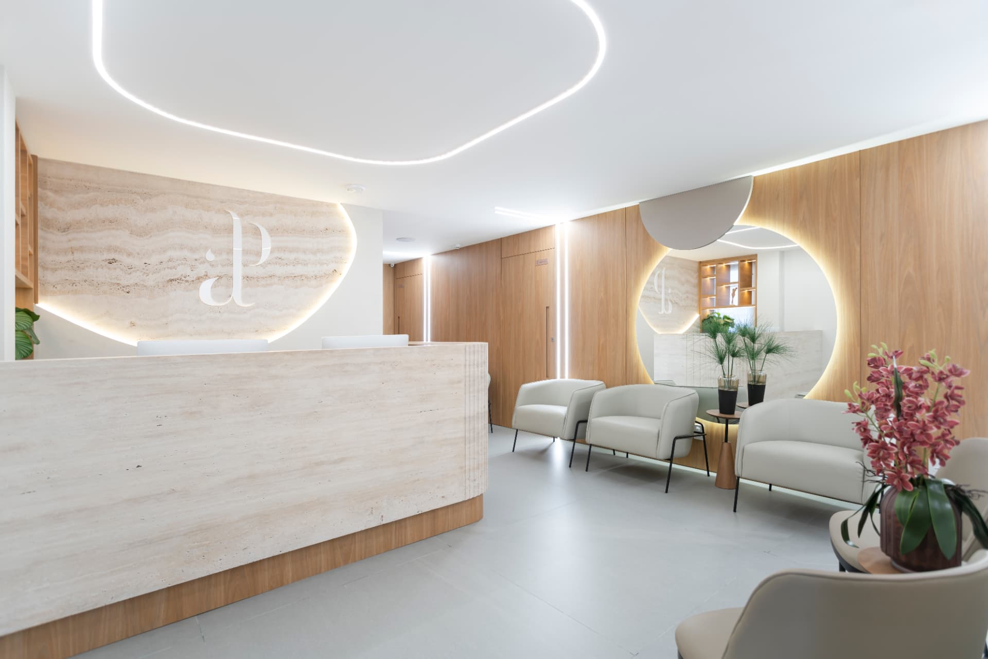 Recepção do Instituto Além da Plástica com balcão em travertino, marcenaria em madeira e iluminação embutida